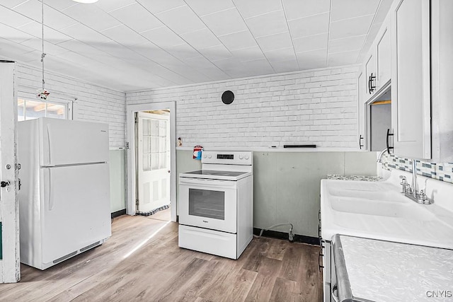 kitchen featuring light wood finished floors, white cabinetry, white appliances, brick wall, and light countertops