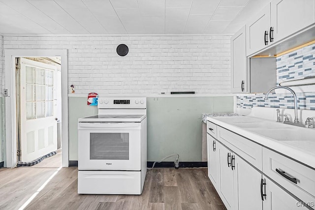 kitchen featuring white electric range oven, light wood-type flooring, and brick wall