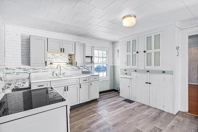 kitchen featuring glass insert cabinets, range with electric cooktop, light wood-type flooring, and a sink