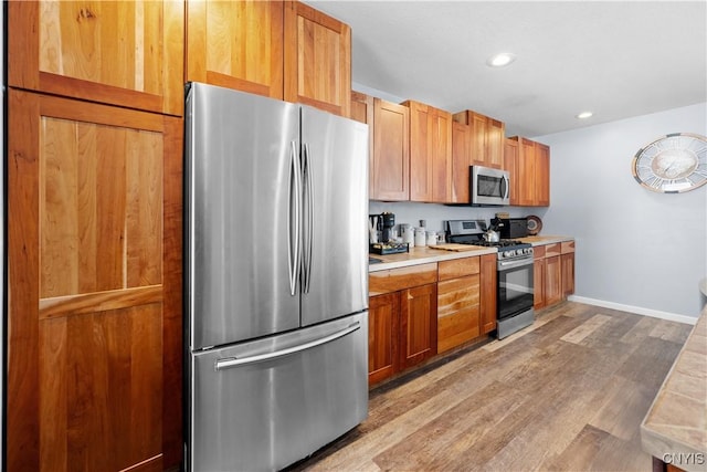 kitchen featuring baseboards, light wood-style flooring, recessed lighting, stainless steel appliances, and light countertops