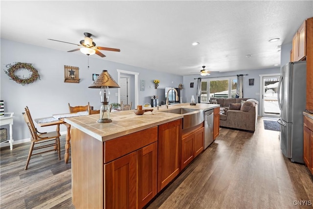 kitchen with a sink, stainless steel appliances, dark wood-type flooring, tile counters, and open floor plan