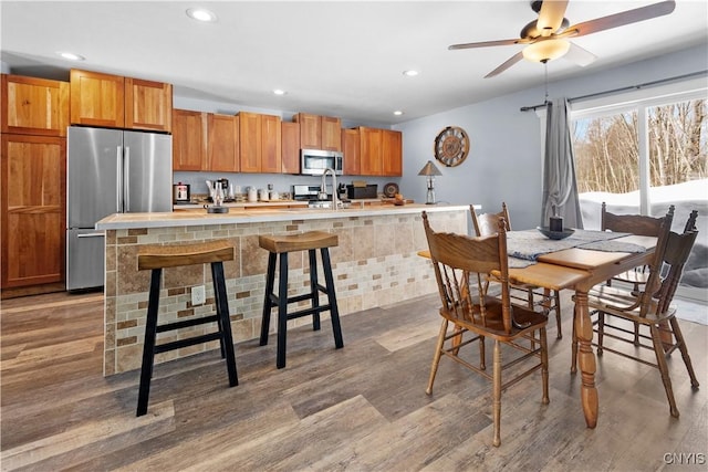 kitchen featuring light countertops, an island with sink, wood finished floors, and appliances with stainless steel finishes