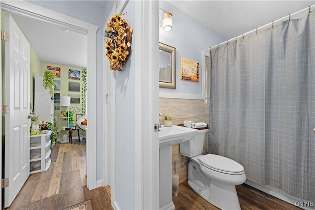 bathroom featuring a shower with shower curtain, wood finished floors, a wainscoted wall, tile walls, and toilet