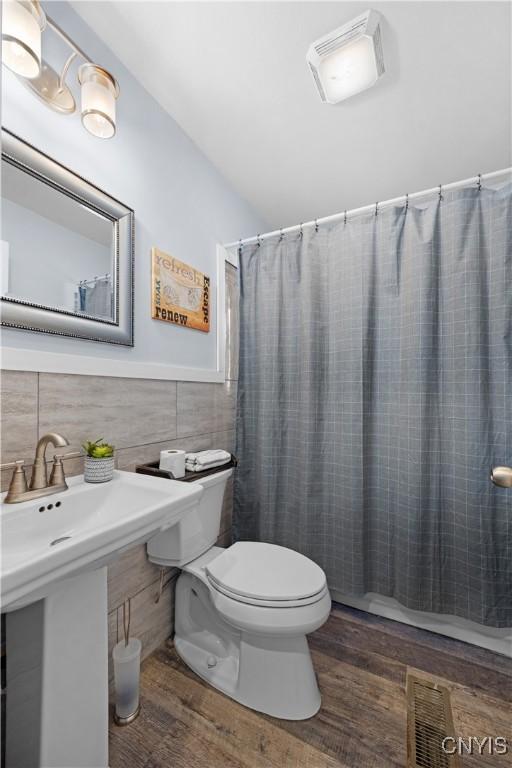 full bathroom with a wainscoted wall, toilet, a shower with curtain, wood finished floors, and tile walls