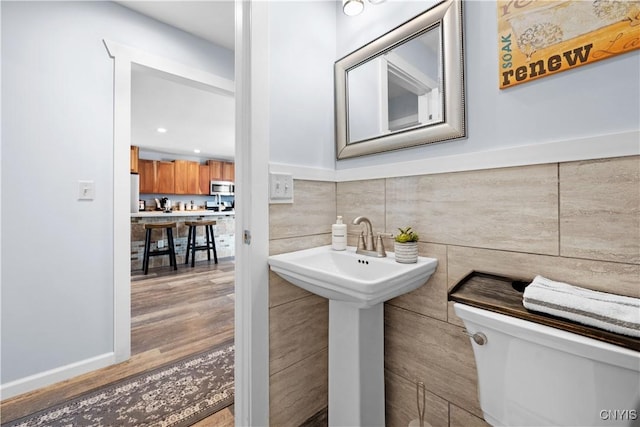 half bathroom featuring toilet, tile walls, and wood finished floors