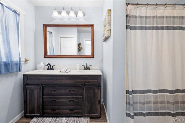 full bath with double vanity, a shower with curtain, baseboards, and a sink