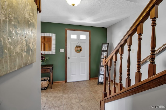 entryway with light tile patterned flooring, stairway, a textured ceiling, and baseboards