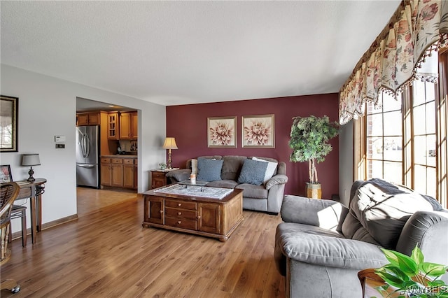 living area with light wood finished floors, a textured ceiling, and baseboards