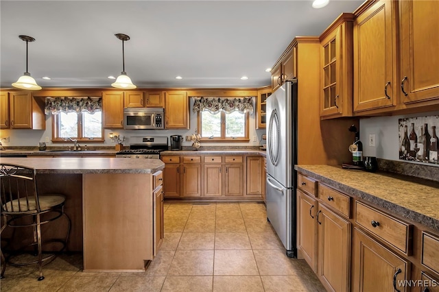 kitchen with dark countertops, light tile patterned floors, brown cabinets, appliances with stainless steel finishes, and a kitchen breakfast bar