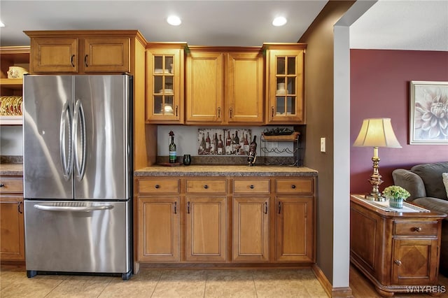 kitchen featuring glass insert cabinets, light tile patterned floors, brown cabinets, and freestanding refrigerator