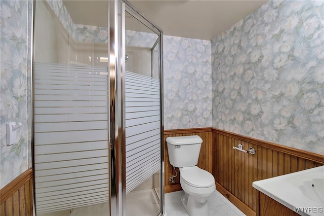 bathroom featuring a wainscoted wall, toilet, a shower stall, and wallpapered walls