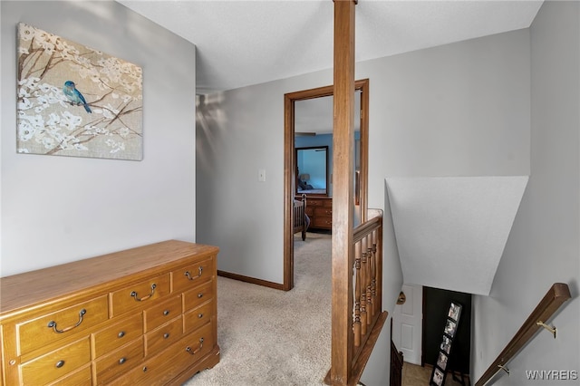 corridor with an upstairs landing, light colored carpet, and baseboards