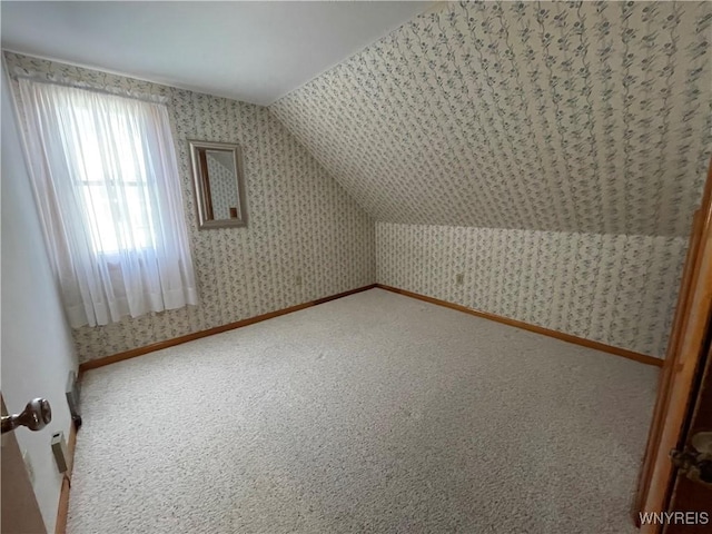 additional living space featuring wallpapered walls, lofted ceiling, carpet flooring, and baseboards