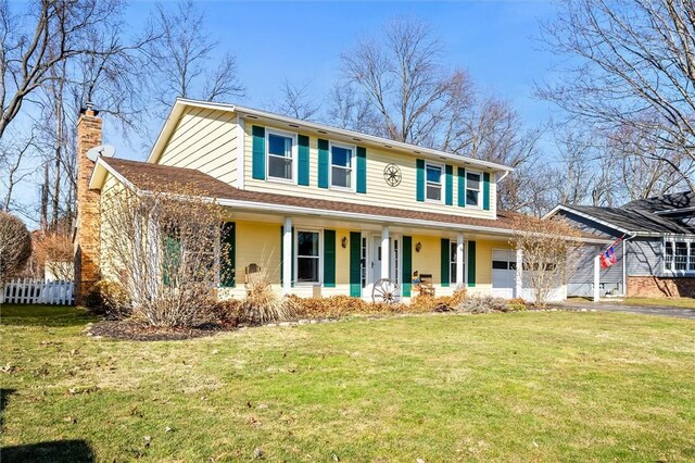 view of front of home featuring driveway, a front lawn, covered porch, an attached garage, and a chimney