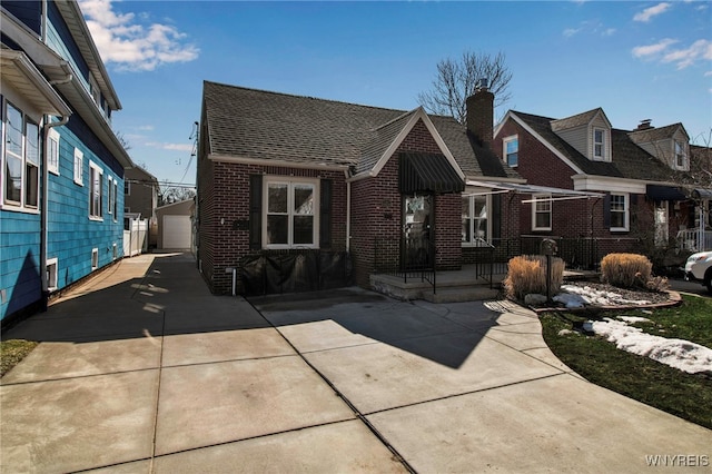 view of front facade featuring an outbuilding, brick siding, and a shingled roof