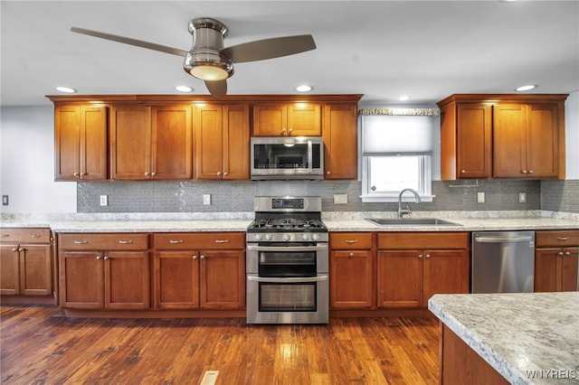 kitchen with dark wood-type flooring, a sink, backsplash, appliances with stainless steel finishes, and brown cabinetry