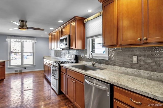 kitchen with brown cabinetry, visible vents, dark wood-style flooring, a sink, and stainless steel appliances