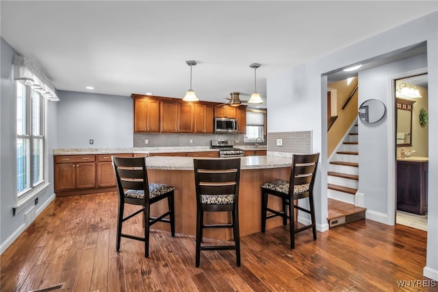 kitchen featuring dark wood-style floors, a sink, decorative backsplash, stainless steel appliances, and brown cabinets