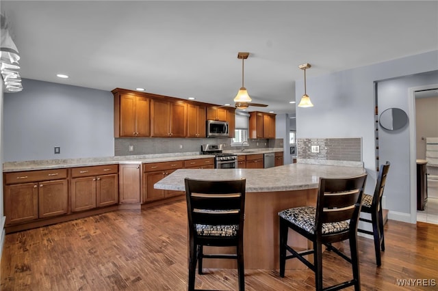 kitchen featuring a sink, dark wood finished floors, stainless steel appliances, brown cabinetry, and light countertops