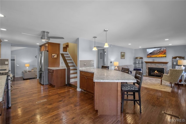 kitchen featuring open floor plan, a breakfast bar, a stone fireplace, brown cabinets, and stainless steel appliances