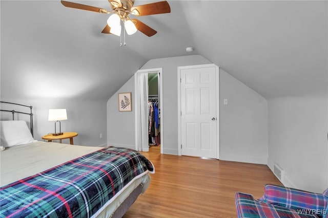 bedroom featuring baseboards, wood finished floors, a spacious closet, and vaulted ceiling