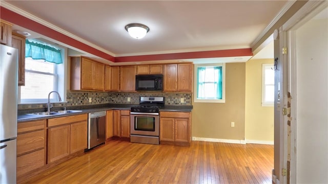 kitchen featuring a sink, dark countertops, stainless steel appliances, light wood finished floors, and decorative backsplash