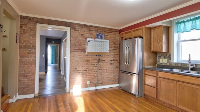 kitchen with brick wall, light wood-type flooring, freestanding refrigerator, and a sink