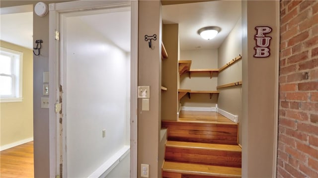 staircase with wood finished floors, baseboards, and brick wall