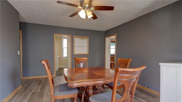 dining area featuring ceiling fan, baseboards, light wood finished floors, and a textured ceiling