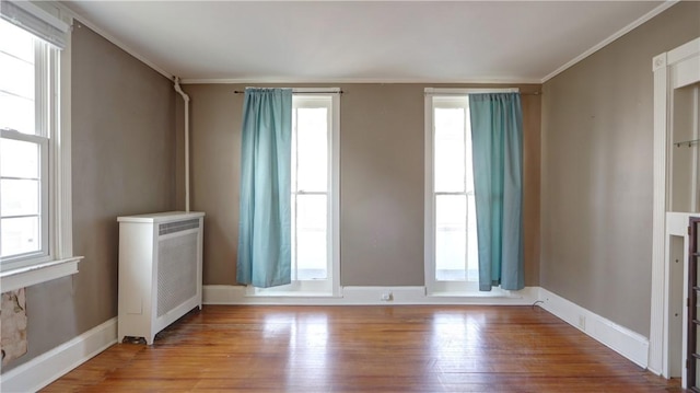 unfurnished room featuring plenty of natural light, wood finished floors, and radiator heating unit