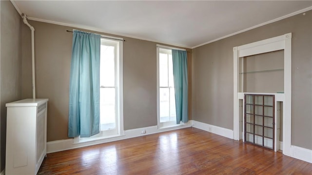 spare room featuring crown molding, wood finished floors, and baseboards