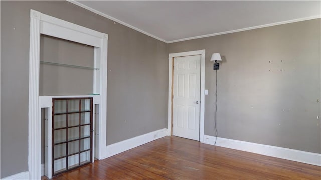 empty room with wood finished floors, baseboards, and ornamental molding