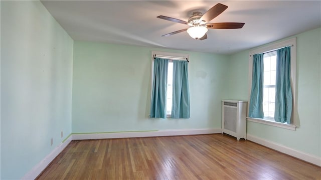 empty room featuring a ceiling fan, radiator heating unit, baseboards, and wood finished floors