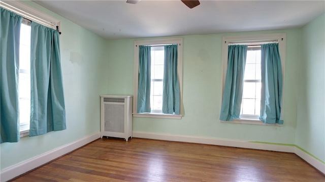 unfurnished room featuring radiator, wood finished floors, baseboards, and ceiling fan