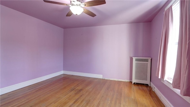 spare room featuring ceiling fan, baseboards, radiator heating unit, and light wood-style floors