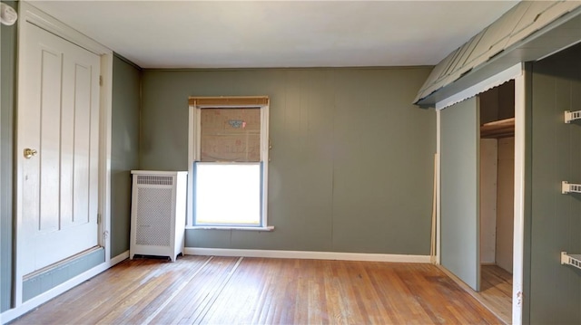 unfurnished bedroom featuring radiator, wood finished floors, and baseboards