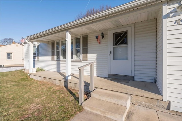 view of exterior entry featuring a yard and covered porch