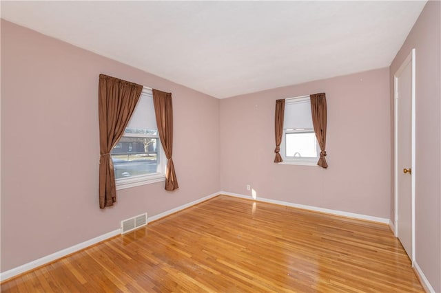 empty room featuring light wood-type flooring, visible vents, and baseboards