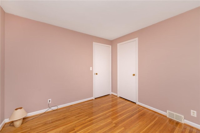 spare room with light wood-style floors, visible vents, and baseboards