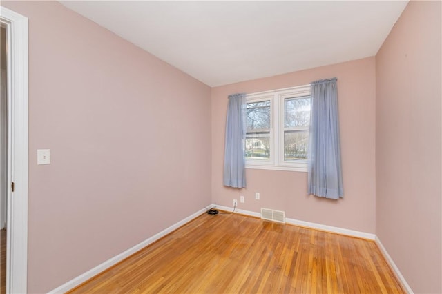 empty room with visible vents, light wood-type flooring, and baseboards