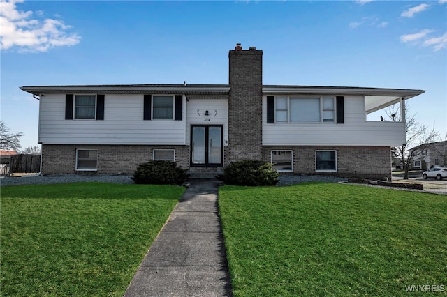 bi-level home with french doors, brick siding, a chimney, and a front yard