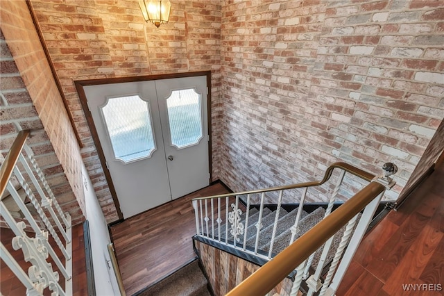 foyer with wood finished floors, stairway, french doors, and brick wall