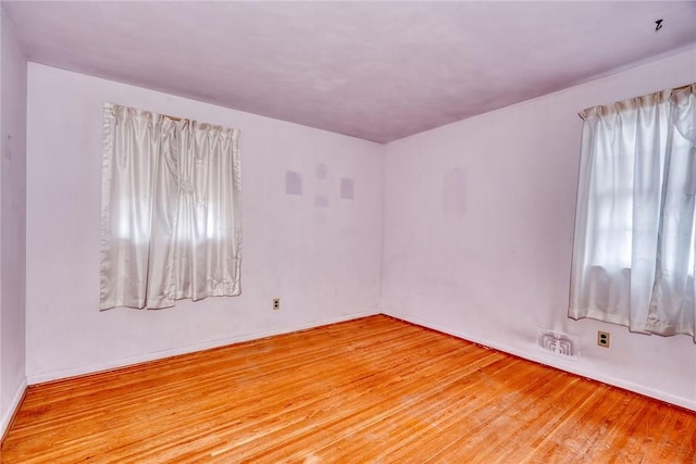 unfurnished room with light wood finished floors, visible vents, and baseboards