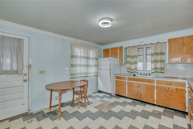 kitchen featuring light countertops, light floors, brown cabinets, and freestanding refrigerator