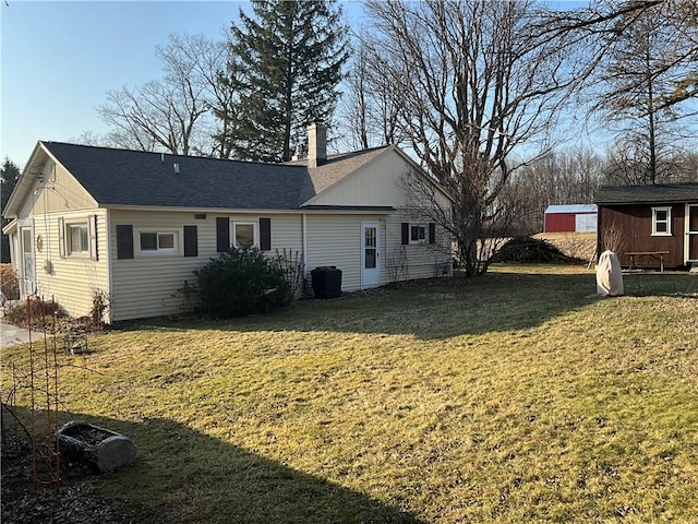 view of side of property with an outdoor structure, a chimney, a yard, and a shingled roof