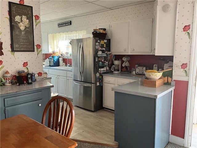 kitchen with a sink, a drop ceiling, white cabinetry, freestanding refrigerator, and wallpapered walls