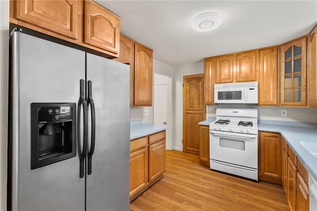 kitchen with white appliances, brown cabinets, light countertops, glass insert cabinets, and light wood-type flooring