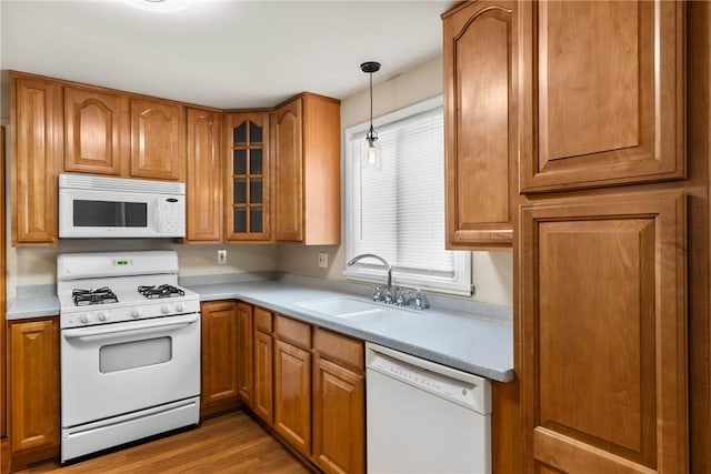 kitchen with a sink, decorative light fixtures, white appliances, brown cabinetry, and glass insert cabinets