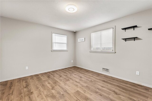 spare room with light wood finished floors, visible vents, and baseboards