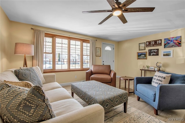 living room featuring baseboards, light wood-type flooring, and ceiling fan